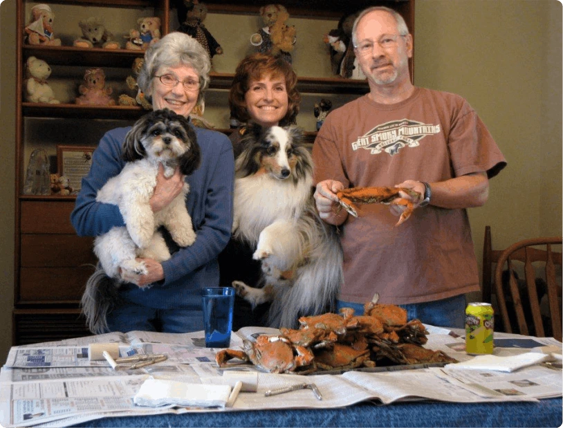 Family at a crab table, two holding dogs and one holding a steamed crab