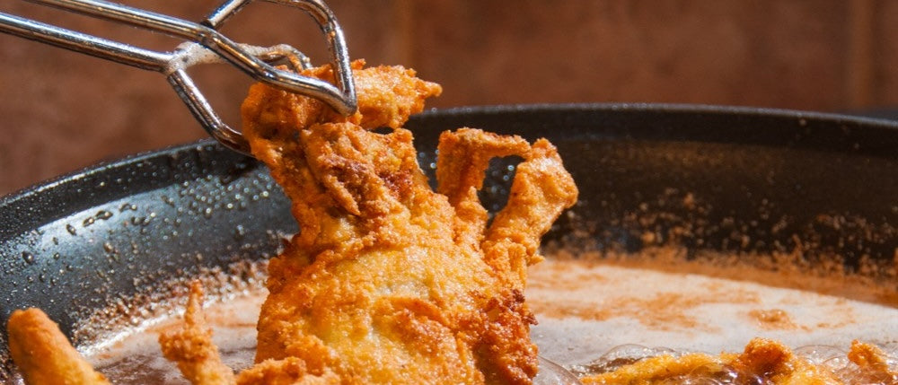 Battered soft shell crab lifted with tongs from frying oil