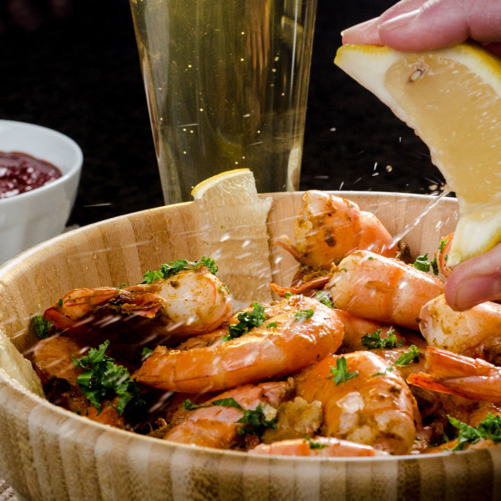 Seasoned jumbo Gulf shrimp in a wooden bowl, lemon being squeezed over