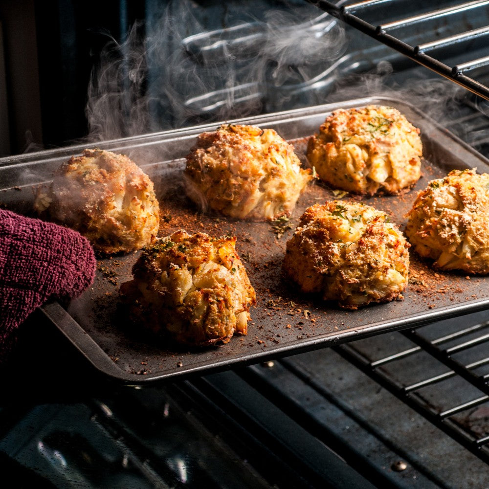 Six jumbo lump crab cakes coming out of the oven on a baking sheet