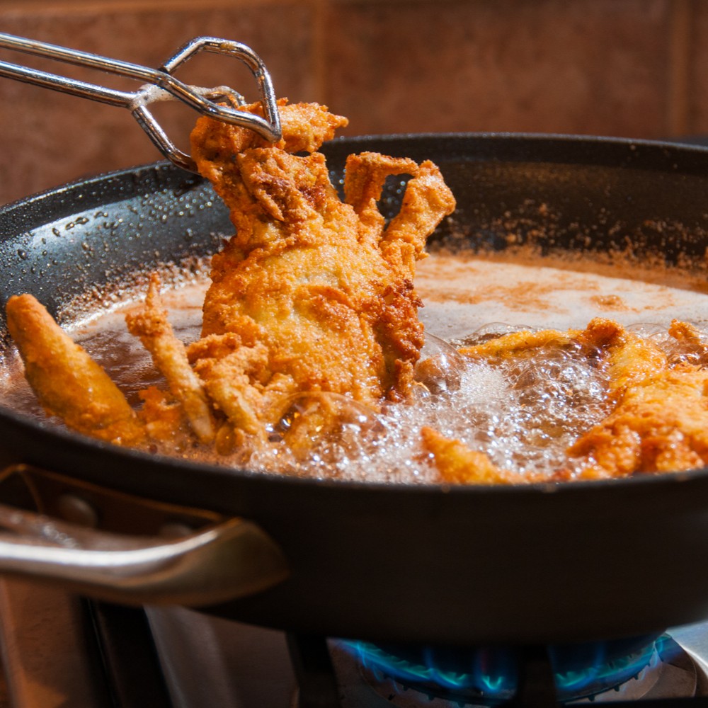 Prime soft shell crab lifted golden from hot frying oil with tongs