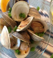 Steamed topneck clams, opened, in a glass bowl with scallions
