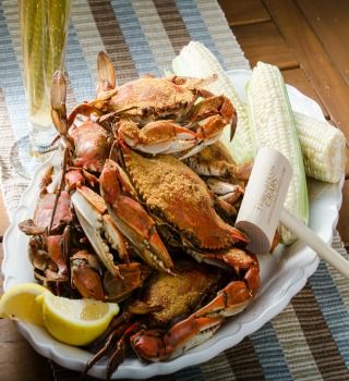 Steamed premium blue crabs on a platter with corn, lemon and a mallet