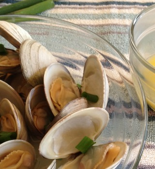 Steamed littleneck clams, opened, in a glass bowl with scallions