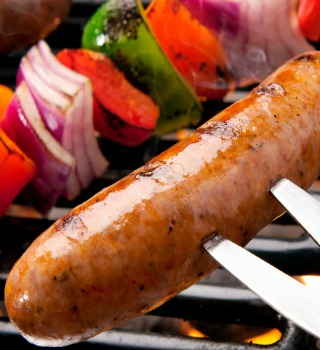 Grilled Cajun sausage on a fork beside vegetable skewers
