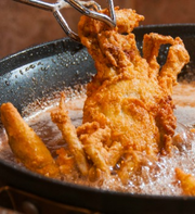 Slab soft shell crab, battered and fried, held by tongs over oil